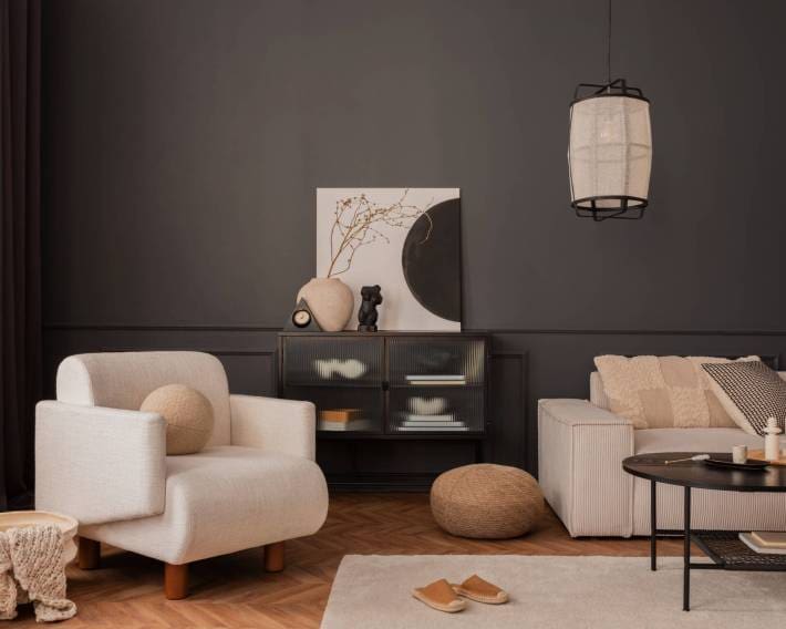 Living room interior with white armchair, beige modular sofa, black coffee table, rug, pillows, slippers, vase with dried flowers, dark wall, lamp and personal accessories. Home decor. Template.